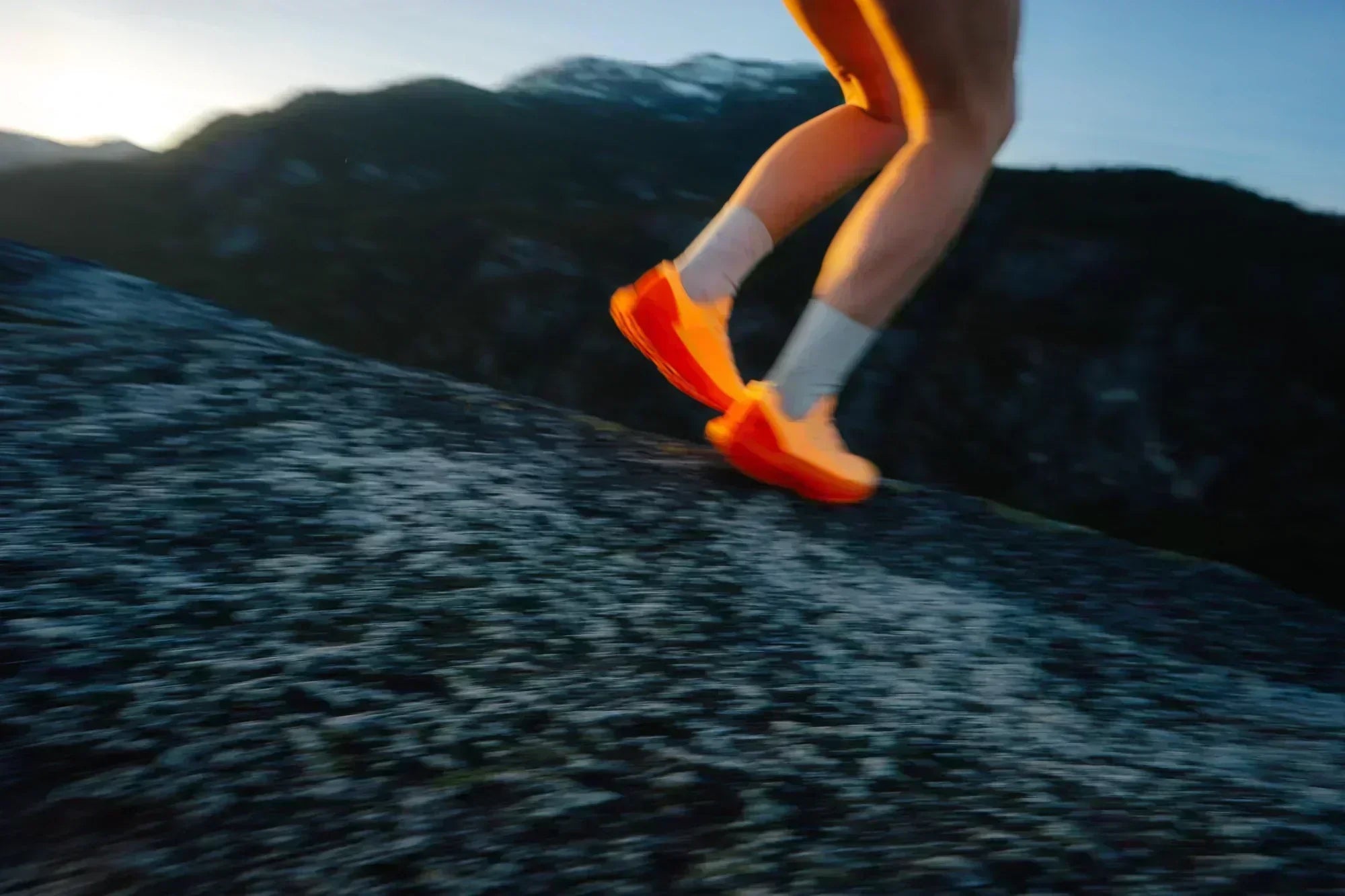 Runner wearing bright orange trail shoes climbing steep rock at dusk in the mountains