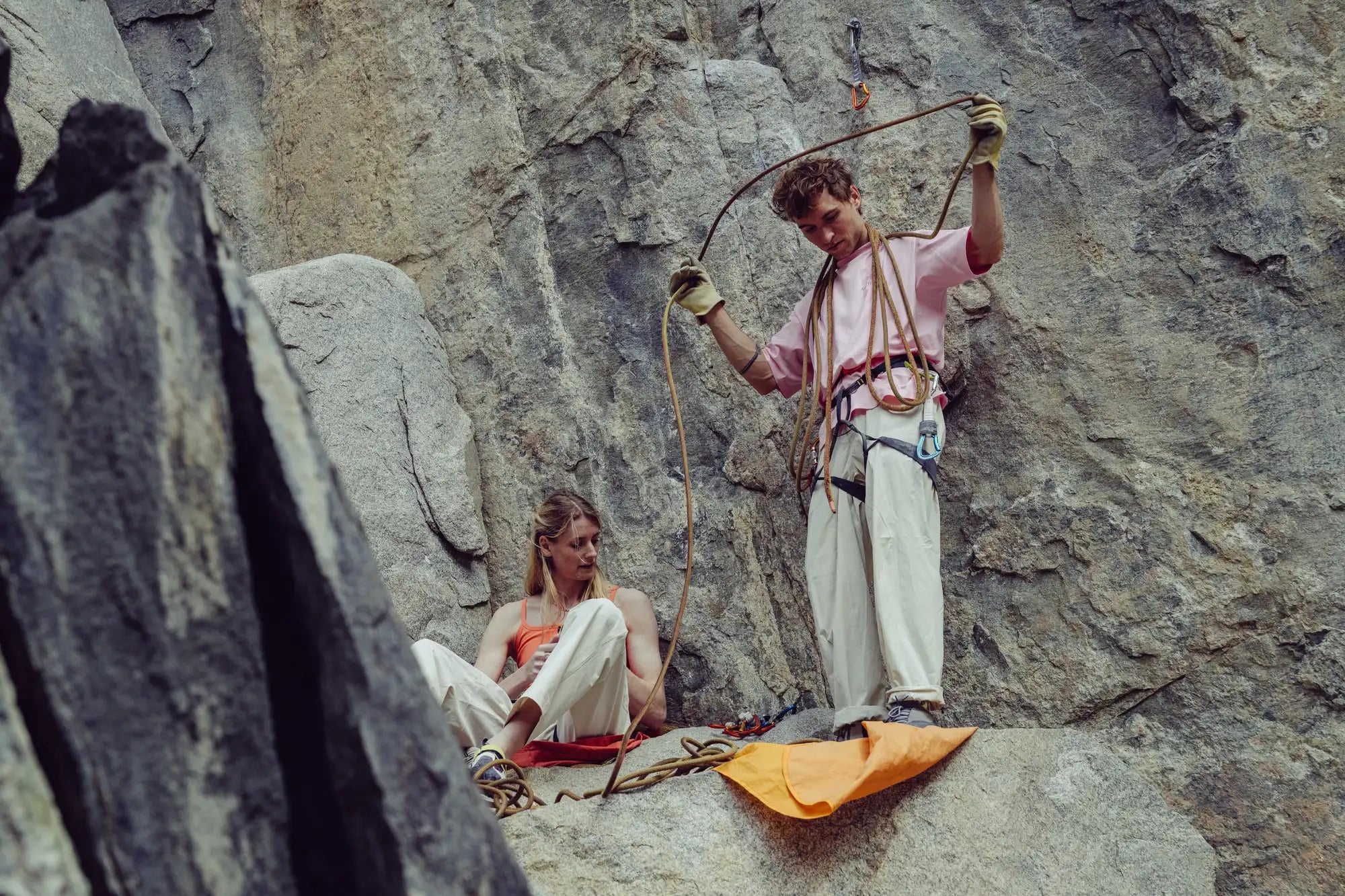 Two rock climbers on a rocky cliff, one holding a rope.