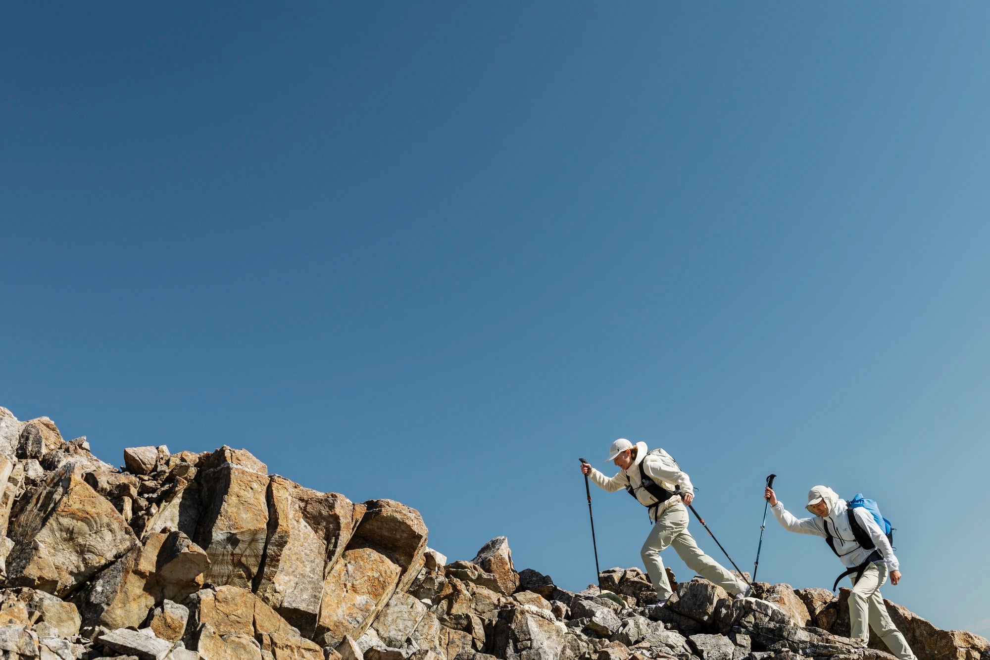 Two hikers wearing windbreakers on a rocky mountain peak with clear blue sky