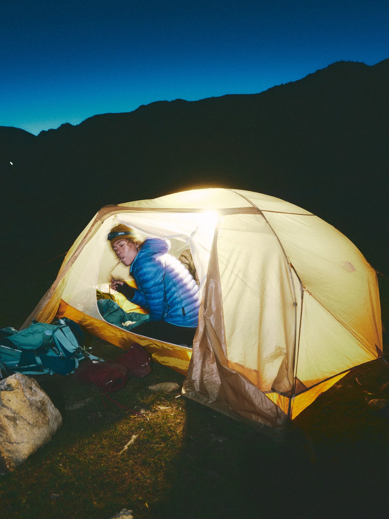 Person inside a illuminated camping tent in a mountainous area at night