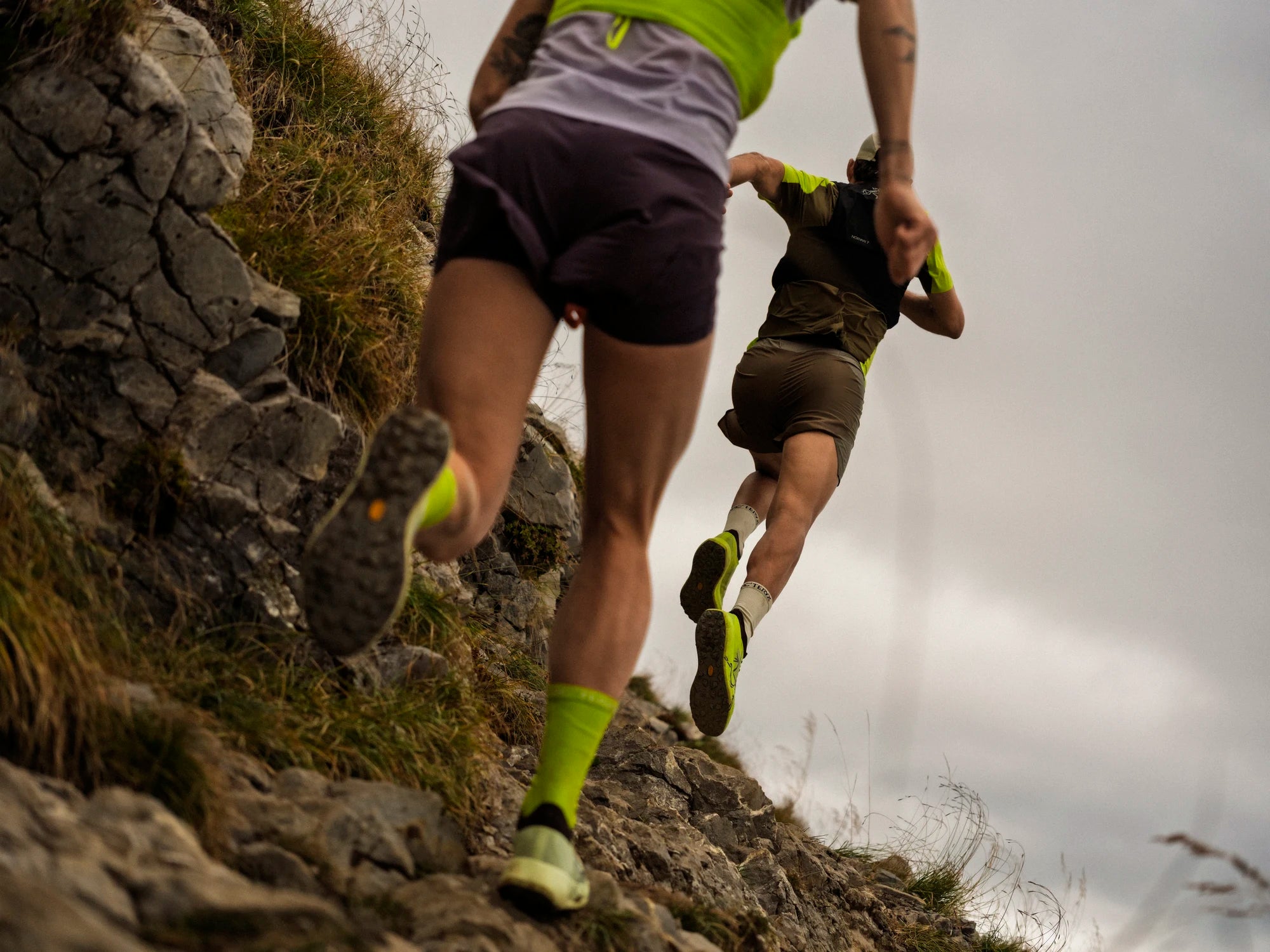 Two trail runners on a rocky trail wearing trail runnings shoes and vests