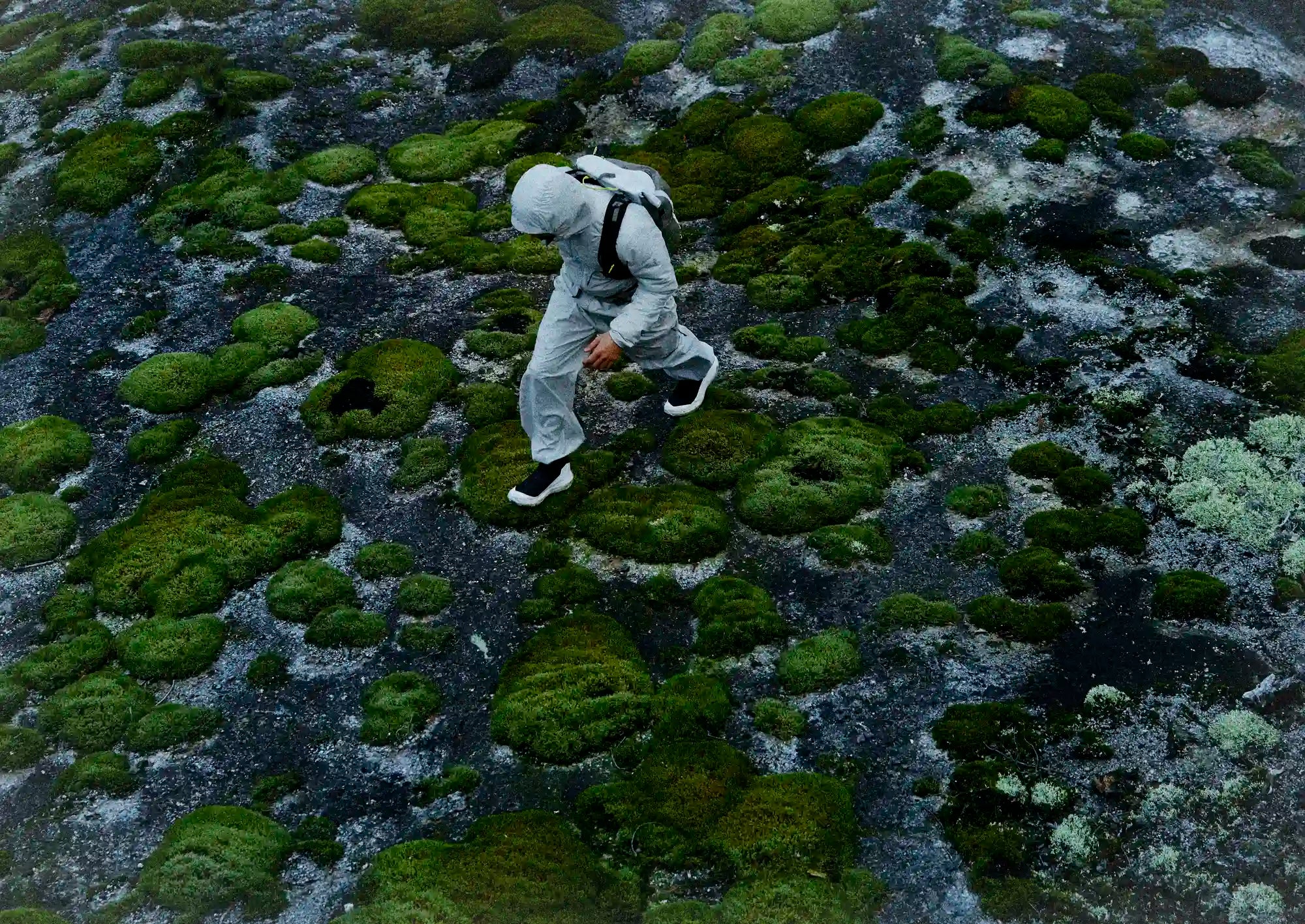 Person in a white suit hiking on a moss-covered surface